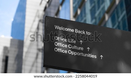 Welcome back to office life on a black city-center sign in front of a modern office building	