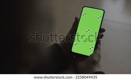 old female hands holding smartphone with green screen over wood vintage table with dim window light