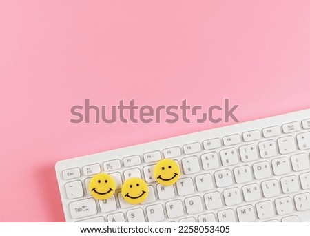 Top view or flat lay of threes yellow circle smiling faces  on white computer keyboard on pink  background.