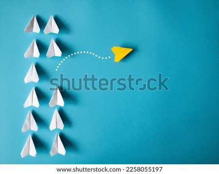 Yellow paper airplane origami leaving other white airplanes on blue background with customizable space for text. Leadership skills concept Royalty-Free Stock Photo #2258055197