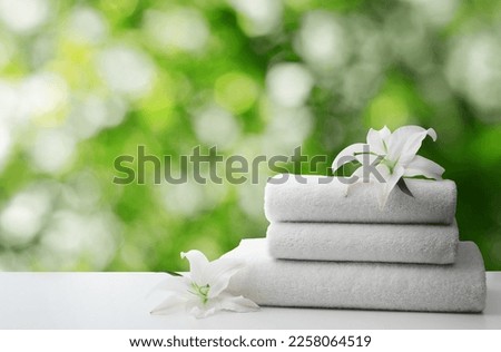 Spa holiday. Stack of fresh towels with flowers on table against blurred green background, space for text Royalty-Free Stock Photo #2258064519