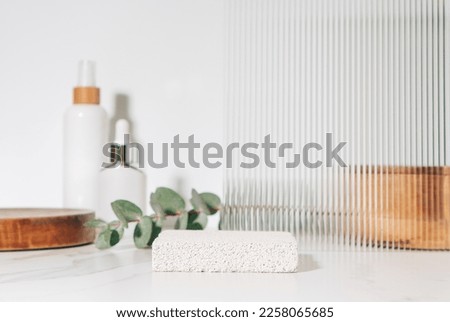 Spa and beauty product presentation scene made with porous stone podium near the cosmetic tubes and accessories on white bathroom shelf. Royalty-Free Stock Photo #2258065685