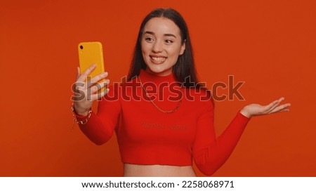 Pretty young woman influencer blogger taking selfie on smartphone, communicating video call online, recording new social media vlog story for subscribers. Girl isolated on red studio background