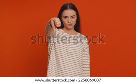 Dislike. Upset unhappy pretty woman in pullover showing thumbs down sign gesture, expressing discontent, disapproval, dissatisfied, dislike. Young adult girl. Indoor studio shot on red background Royalty-Free Stock Photo #2258069007