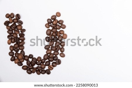 U is a capital letter of the English alphabet made up of natural roasted coffee beans that lie on a white background. Plenty of space to put text or pictures, top view and studio photography.