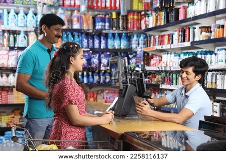 Indian father and daughter, after shopping in supermarket getting the billing done on the billing counter.  Royalty-Free Stock Photo #2258116137