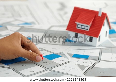 Hand holding red pin pointing to cadastral map to decide to buy land. real estate concept with vacant land for building construction and housing subdivision for sale, rent, buy, investment Royalty-Free Stock Photo #2258143363