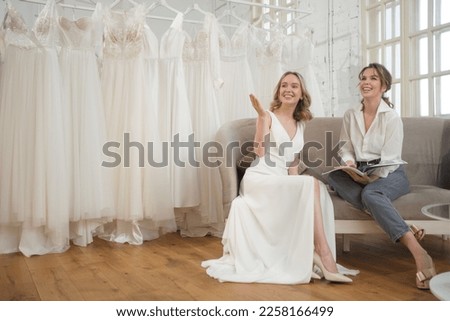 Woman trying on wedding dress with female friends having fun and taking photographs.