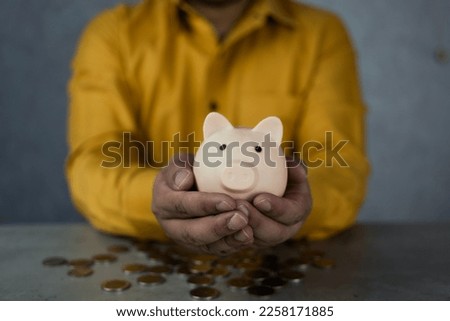 Piggy bank in form of pink pig in hands of joyful contented man in yellow shirt on light gray background. Cropped image. Save money