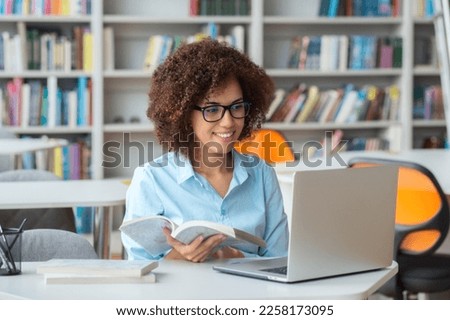 Young African American woman teacher uses laptop for video conference sitting in university or school library. Online lessons or remote education, teaching students. E-learning concept