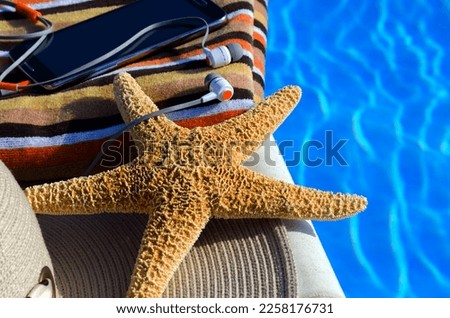 Women's hat, mobile phone and headphones next to the pool. Starfish with women's accessories.