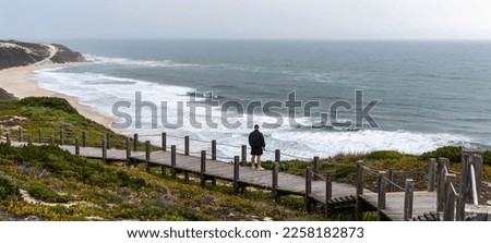 Man tourist early spring on wooden walkway to beautiful sand beach sea view near Pataias, Portugal.
