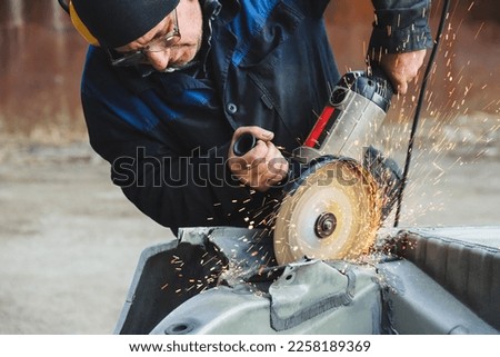 Worker saws metal with an old angle grinder. Selective focus. Outdoors. Flying sparks. Industrial concept