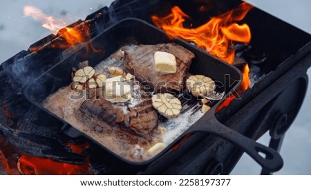 Steak on fire. Cast iron frying pan. Fresh meat. Open fire. Barbecue. Firewood.