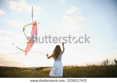 Little cute 7 years old girl running in the field with kite on summer day.