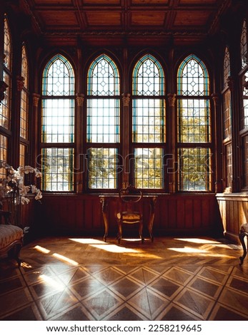 Sun shining into an old wooden room with high, beautiful windows and a single table in the center in a castle Royalty-Free Stock Photo #2258219645