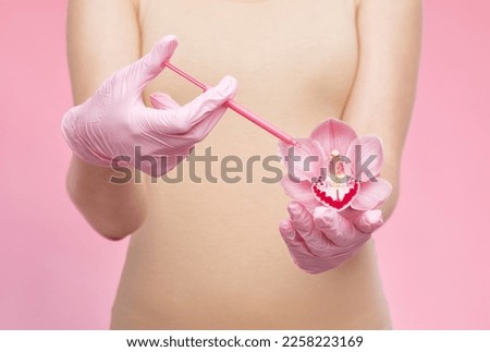 A woman holds a pink orchid in her hands and makes injections for rejuvenation. The concept of plastic surgery.