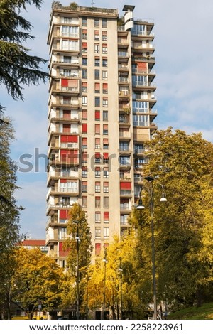 One multi-story residential building in the city among green trees against a light blue sky background