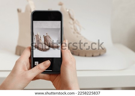 A woman takes a picture of new shoes on a mobile phone at home. Mobile shooting for goods for sale. Blogger and stylist photographing clothes. Reusing unnecessary things