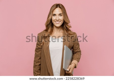 Young happy fun successful employee business woman 30s she wear casual brown classic jacket hold closed laptop pc computer look aside on workspace area isolated on plain pastel light pink background
