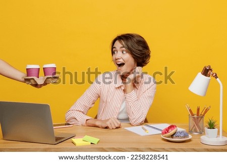 Young amazed employee business woman wearing shirt given takeaway paper cup coffee to go sit work at office desk with pc laptop isolated on plain yellow color background. Achievement career concept