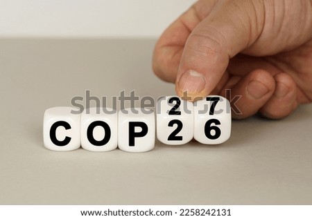 On a gray surface are white cubes with the inscription - COP26 to COP27. Two dice in hand. Technology concept Royalty-Free Stock Photo #2258242131