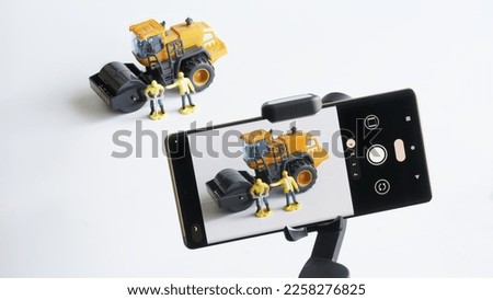 Mobile phone on gimbal selfie stick for photo-video filming toy construction machinery and workers. Concept of observing and monitoring the work of construction workers and journalism. Close-up