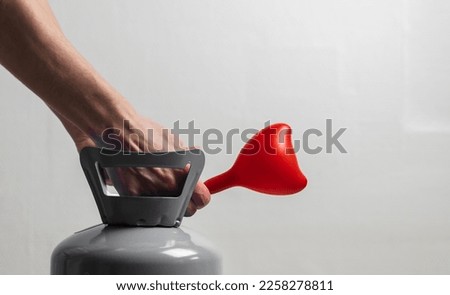 Hands of a young caucasian man inflate a red heart balloon with a helium compressor on a white background,side view close-up.Valentine's day concept,preparation,holidays.