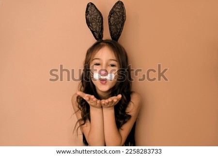 A beautiful attractive girl with ears decorated with face paints in rabbit. A child in the form of an animal sends an air kiss. Easter Bunny