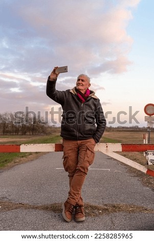 middle aged man wearing winter clothes taking a selfie in a country road - concept of people in recreation