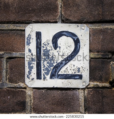weathered house number twelve. Black numerals on a white plate.