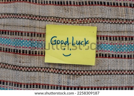 handwriting of the message "Good luck!" and smiley face on yellow sticky note with colorful curtain background. Top view Wallpaper of aesthetic encouraging words on a yellow stick note