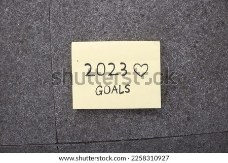writing 2023 new year resolution goal on yellow sticky note with love emoji on gray background. Wallpaper words of encouragement 2023. A small motivational note for the year 2023 resolution