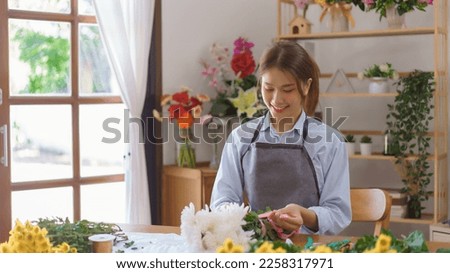 Florist concept, Woman florist making white chrysanthemum bouquet and tie ribbon at flower shop.