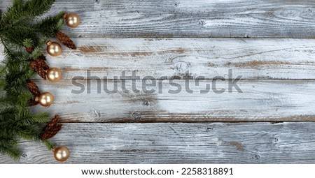 Christmas decoration with real fir branches plus gold ball ornaments forming left border on white aged wood background 