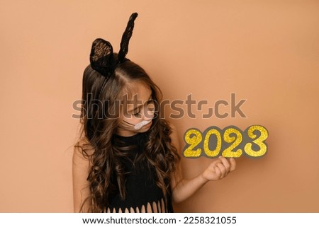 A girl dressed up as a black rabbit holds in her hands the golden numbers of the new year 2023. The year of the bunny according to the Eastern Chinese calendar