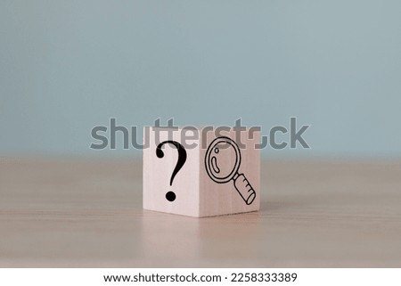 The wooden cube block with an illustration magnifying glass to analyze the question mark sign is isolated on the table. Problems and root cause analysis concept. Define problems to find solutions.  Royalty-Free Stock Photo #2258333389