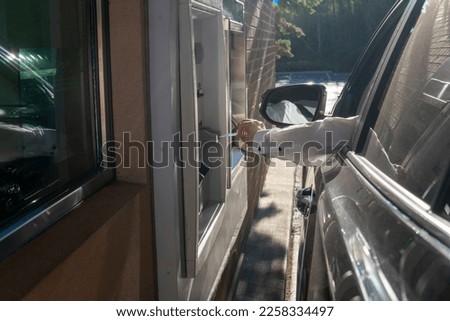 Man's hand from the car with card near ATM. Man using - ATM drive through. Money withdrawal Royalty-Free Stock Photo #2258334497
