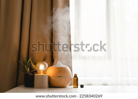 Aromatherapy concept. Aroma oil diffuser on the table against the window. Air freshener. Ultrasonic aroma diffuser for home Royalty-Free Stock Photo #2258340269