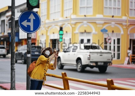 Tourists use digital cameras to take pictures at beauty of city streets old town in old phuket town,Thailand. Woman wearing yellow top and wide-brimmed hat, sling an orange backpack walking happily. 