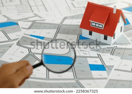 Man holding magnifier on cadastre map search for assesses to buy the land lands. real estate concept with vacant land for building construction and housing subdivision for sale, rent, buy, investment Royalty-Free Stock Photo #2258367325