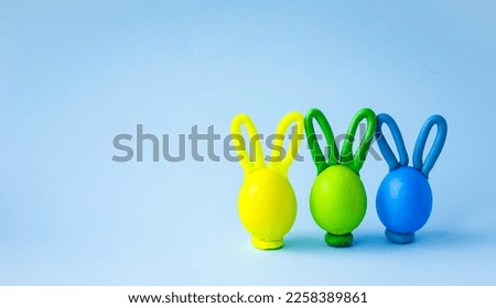 Cheerful Easter eggs on a blue background.  Multi-colored eggs with plasticine ears.  Craft colored Easter bunnies.  Children's postcard.  Front view.  Space for copy text.