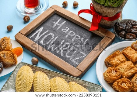 Chalkboard with text HAPPY NOWRUZ and treats on blue background, closeup