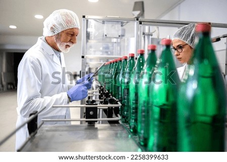 PET packaging bottling plant and workers in white coat controlling water production. Royalty-Free Stock Photo #2258399633