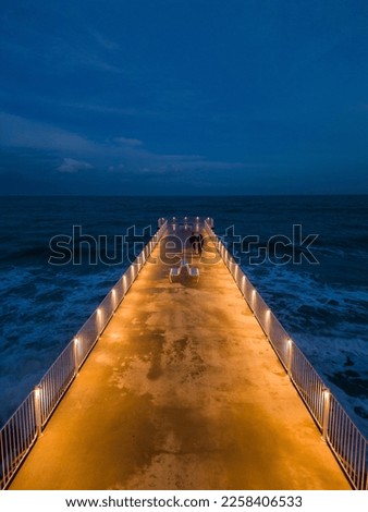 illuminated pier with dramatic sky over stormy dark sea at evening aerial view, Varna Bulgaria