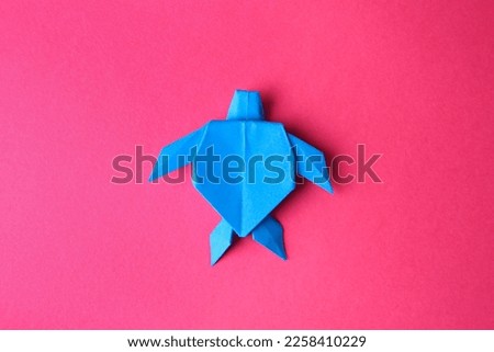 Origami art. Handmade light blue paper turtle on pink background, top view
