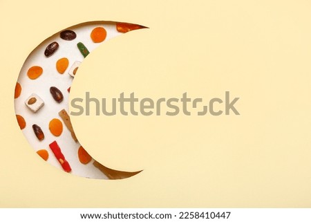 Sweets visible through cut color paper in shape of crescent for Ramadan