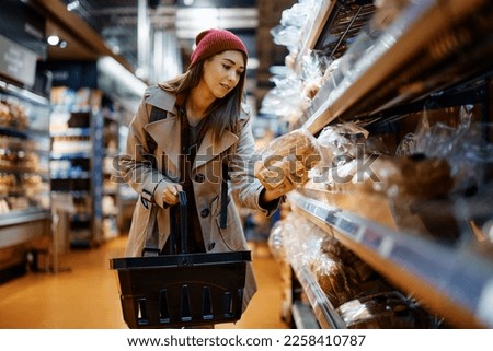 Young woman choosing bread while buying groceries in supermarket.  Royalty-Free Stock Photo #2258410787