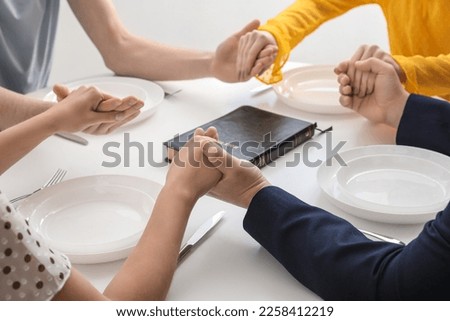 Group of people praying with Holy Bible before dinner in room, closeup