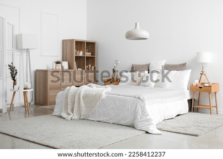 Interior of bedroom with bed, shelving unit, burning candles and houseplants near white wall Royalty-Free Stock Photo #2258412237